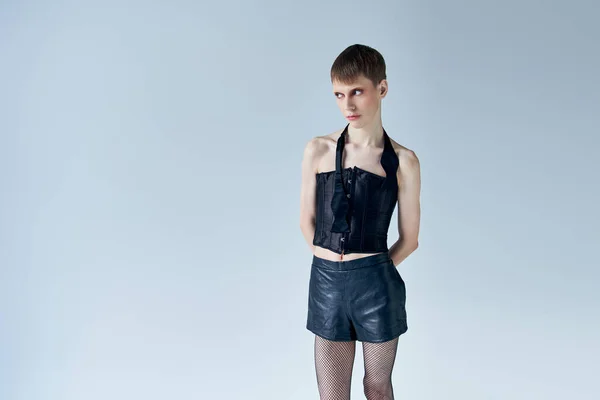 Modello androgino in corsetto nero e pantaloncini che distolgono lo sguardo su grigio, lgbt, moda queer, stile — Foto stock