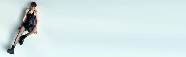 Квір-модель в корсеті і ажурних колготках, що сидять на сірому, lgbt, андрогінний, високий кут зору, банер — стокове фото