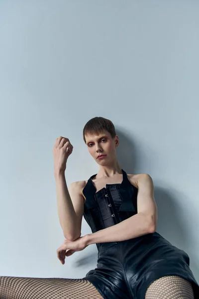 Androgynes Modell in Korsett, Shorts und Netzstrumpfhosen posiert vor grauem Hintergrund, queere Mode, lgbtq — Stockfoto