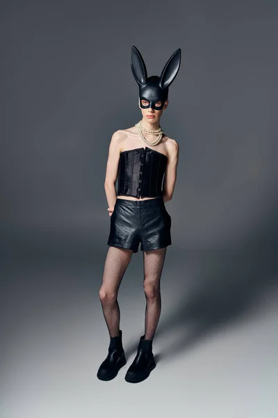 Modello androgino in corsetto nero in posa bdsm maschera coniglietto su sfondo grigio, moda queer, lgbt — Foto stock