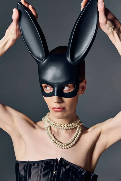 Persona queer in corsetto toccare bdsm maschera coniglietto su grigio, collana di perle, lgbtq, androgino — Foto stock