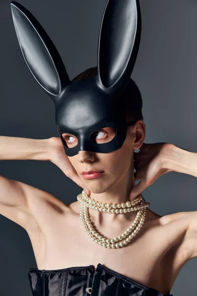 Persona queer in corsetto e nero bdsm maschera coniglietto su grigio, androgino, moda, posa, guardare altrove — Foto stock