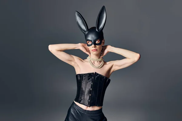 Modello queer in corsetto nero e maschera coniglietto bdsm su grigio, androgino, moda, posa, distogliere lo sguardo — Foto stock