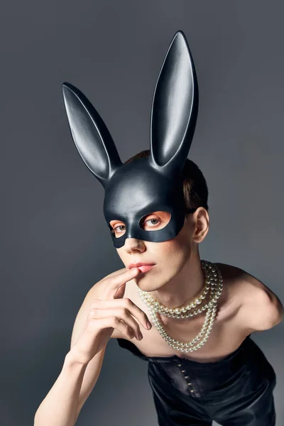 Queer persona in corsetto e bdsm coniglietto maschera posa su grigio, dito vicino alle labbra, moda, guardare la fotocamera — Foto stock