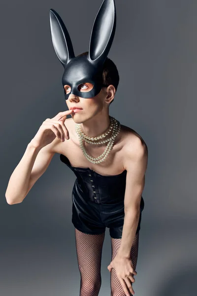 Modèle queer en corset et bdsm lapin masque posant sur gris, doigt près des lèvres, mode, regarder vers le haut — Photo de stock