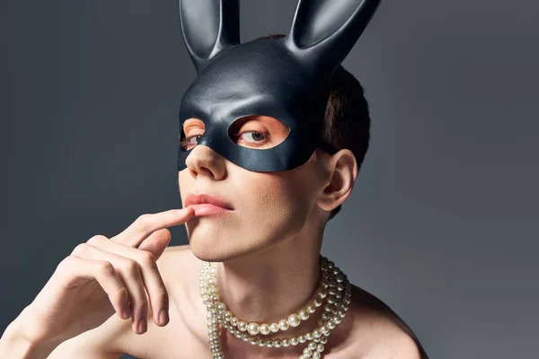 Portrait, queer model in corset and bdsm bunny mask posing on grey, finger near lips, fashion — Stock Photo