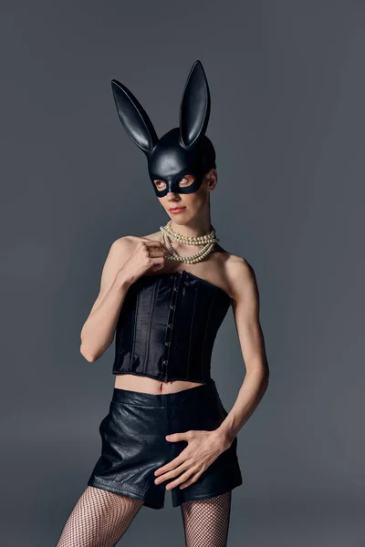 Modello queer in corsetto posa in bdsm maschera coniglietto su grigio, collana di perle, stile provocatorio — Foto stock