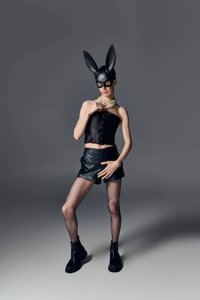 Persona queer in corsetto posa in bdsm maschera coniglietto su grigio, collana di perle, moda provocatoria — Foto stock