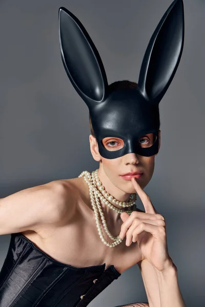 Kühner Blick, provokante queere Person im Korsett posiert in bdsm Hasenmaske auf grauer, kantiger Mode — Stockfoto
