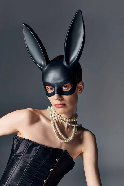 Bold look, genderqueer person in corset posing in bdsm bunny mask on grey, queer fashion, style — Stock Photo