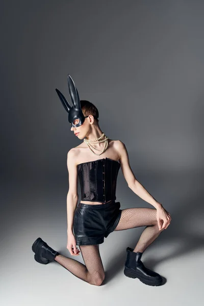 Stile audace, persona genderqueer in corsetto posa in maschera coniglietto bdsm su grigio, moda queer — Foto stock