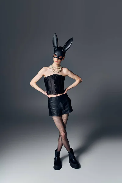 Style, genderqueer person in corset posing in bdsm bunny mask on grey, queer fashion, hands on hips — Stock Photo