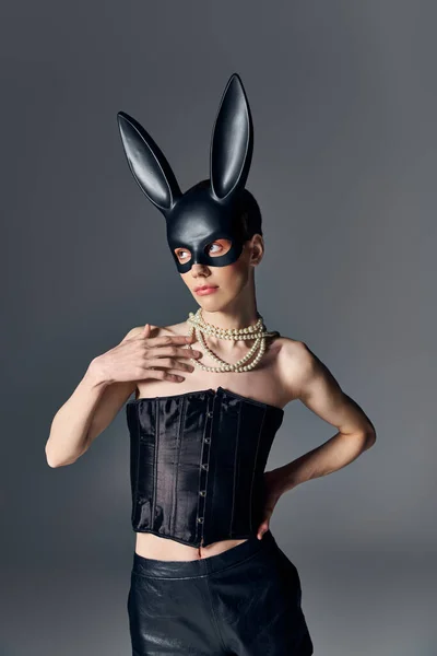 Moda, genderqueer persona in corsetto posa in bdsm maschera coniglietto su grigio, stile queer, mano sul fianco — Foto stock