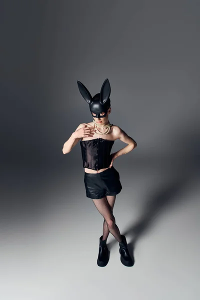 Kühner Blick, genderfluide Person im Korsett posiert in bdsm Hasenmaske auf grau, queerer Stil, Hand auf Hüfte — Stockfoto