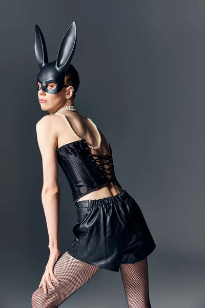 Persona queer in corsetto e pantaloncini, nero bdsm maschera coniglietto posa su grigio, moda, corsetto allacciatura — Foto stock