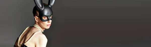 Queer person in korsett und bdsm hasenmaske posiert auf grau, perlenkette, kantige mode, banner — Stockfoto