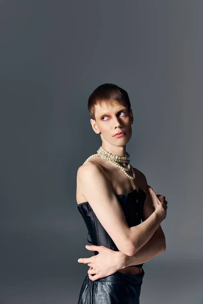 Personne queer en corset noir et collier de perles posant sur fond gris, mode agitée, maquillage — Photo de stock