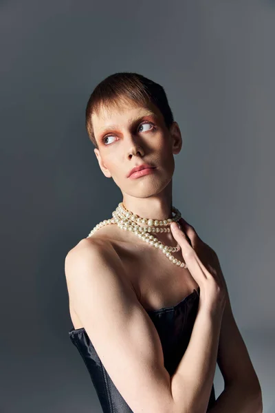 Queer personne en corset noir et collier de perles posant sur fond gris, mode agitée, non binaire — Photo de stock