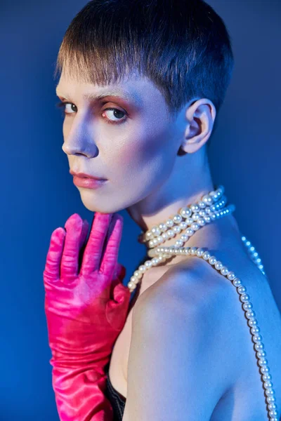 Retrato, persona no binaria en corsé y guantes de color rosa posando sobre fondo azul, modelo queer - foto de stock