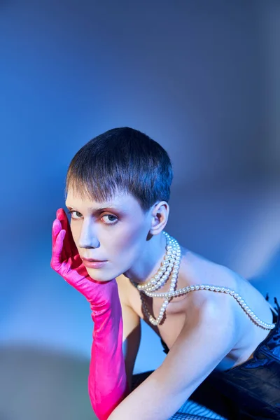 Persona non binaria in corsetto e guanto rosa in posa su sfondo blu, modello queer, espressione di sé — Foto stock