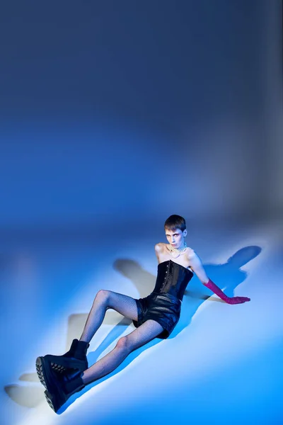 Androgyne en corset et bottes assis sur fond bleu, personne non binaire en gants roses, queer — Photo de stock