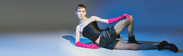 Queer model in fettem Outfit und pinkfarbenen Handschuhen posiert auf blauem Hintergrund, Shorts, nicht binär, Banner — Stockfoto