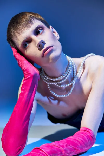 Dreamy queer model in bold outfit and pink gloves posing on blue backdrop, nonbinary, look away — Stock Photo