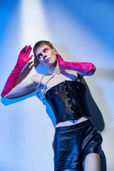 Von oben, merkwürdiges Modell in Korsett und rosa Handschuhen, wegschauend und auf blauem Hintergrund liegend, lgbtq — Stockfoto