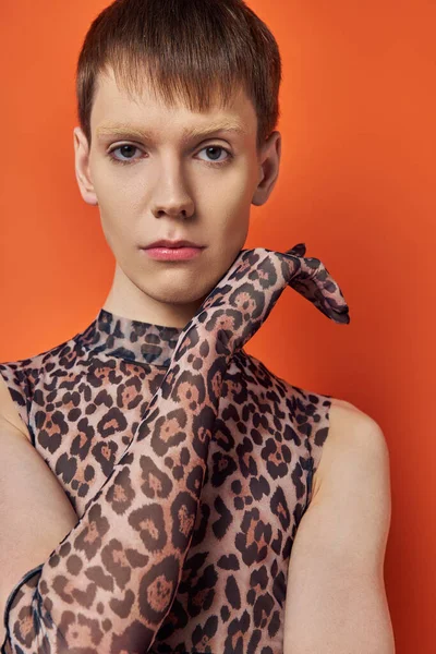 Modelo queer en traje de impresión animal posando sobre fondo naranja, genderfluid en estampado de leopardo - foto de stock