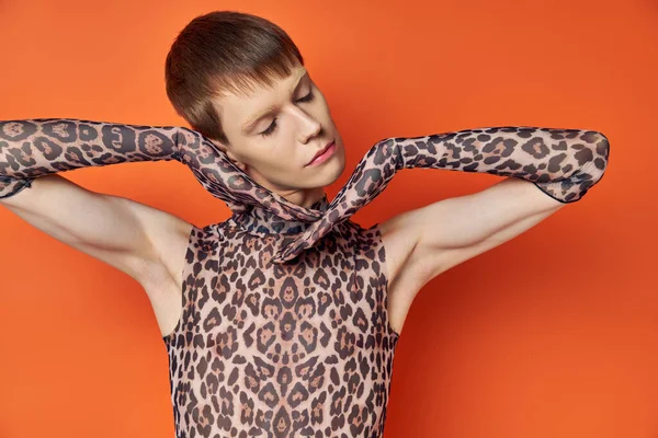 Queer model in animal print outfit posing on orange backdrop, closed eyes, stylish genderfluid — Stock Photo