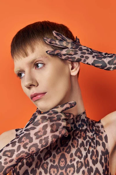 Primer plano del modelo queer en traje de impresión animal posando sobre fondo naranja, género con estilo fluido - foto de stock