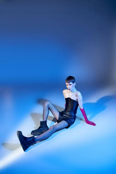 Longueur totale du modèle queer en corset et gants roses assis sur fond bleu, lgbtq, style audacieux — Photo de stock