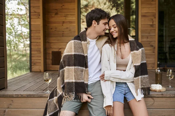 Casal positivo em cobertor sentado com olhos fechados perto de vinho e queijo com casa de verão ao ar livre — Fotografia de Stock