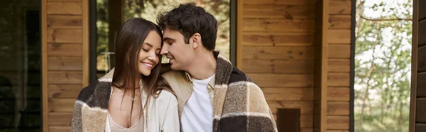 Couple romantique joyeux dans la couverture assis avec les yeux fermés près de la maison de vacances, bannière — Photo de stock