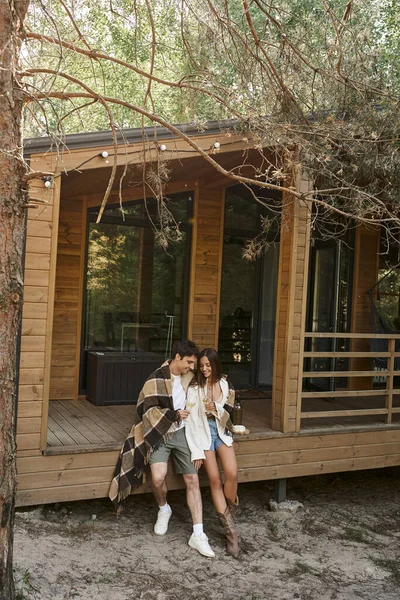 Positiva coppia romantica in coperta che tiene il vino vicino al formaggio mentre si siede sul portico della casa estiva — Foto stock