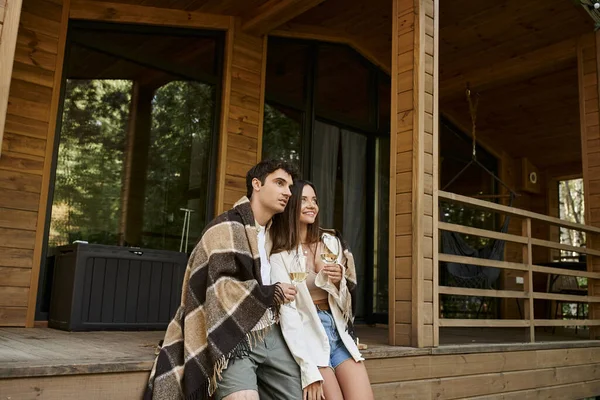 Lächelndes Paar in Decke, Wein haltend und auf der Veranda des Sommerhauses wegschauend — Stockfoto