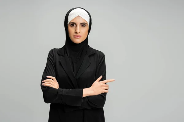 Moderna donna d'affari musulmana in hijab e nero arrossito in piedi con le braccia incrociate su grigio, colpo alla testa — Foto stock
