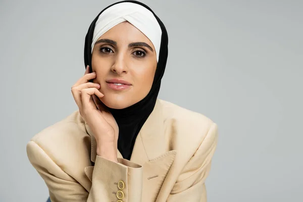 Portrait of modern and trendy muslim businesswoman in hijab and blazer looking at camera on grey — Stock Photo