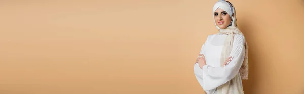 Donna musulmana sorridente in camicetta bianca ed elegante velo in posa con le braccia incrociate sul beige, striscione — Foto stock