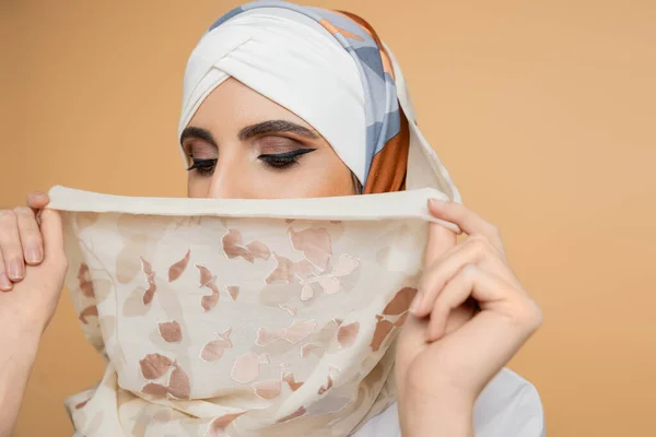 Modest muslim woman with makeup obscuring face with stylish silk headscarf on beige — Stock Photo