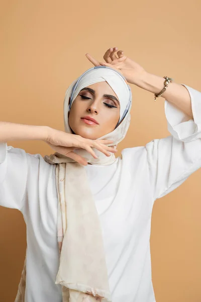 Sensual muslim woman with closed eyes and makeup posing in silk headscarf and white blouse on beige — Stock Photo