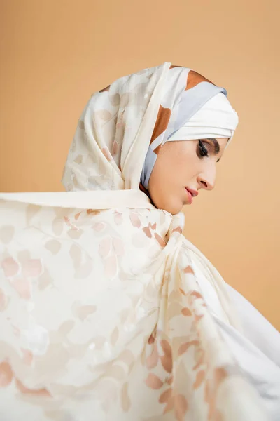 Side view of attractive muslim woman with makeup wearing elegant silk headscarf on beige — Stock Photo