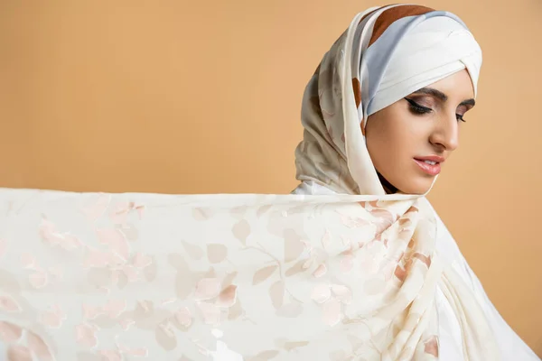 Séduisante femme musulmane avec maquillage portant une écharpe élégante en soie sur beige, style personnel, portrait — Photo de stock