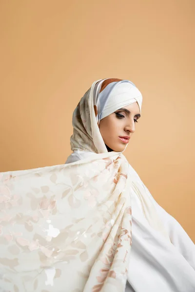 Portrait of glamour middle eastern woman with makeup posing in silk scarf on beige, muslim beauty — Stock Photo