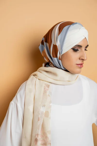 Charming and graceful muslim with makeup, in silk scarf and white blouse standing on beige — Stock Photo