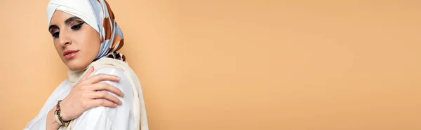 Sensual mulher muçulmana com maquiagem posando em cachecol de seda elegante e blusa branca no bege, banner — Fotografia de Stock