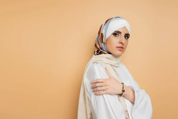 Modern muslim woman with makeup posing in silk scarf and white blouse on beige, self-expression — Stock Photo
