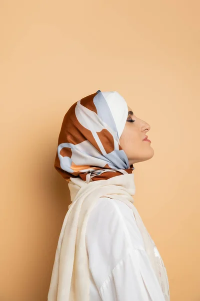 Profilo di attraente donna musulmana in elegante foulard di seta in posa con gli occhi chiusi sul beige — Foto stock