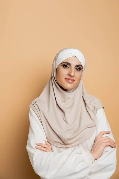 Confident muslim woman in hijab and sweatshirt posing with folded arms, smiling at camera on beige — Stock Photo