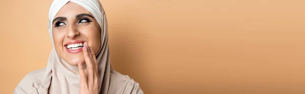 Fröhliche, ausdrucksstarke muslimische Frau im Hijab, die den Mund mit der Hand bedeckt und auf beige lacht, Banner — Stockfoto